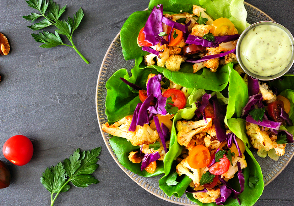 Healthy plant based lettuce wraps with grilled cauliflower, top view over a dark slate background Healthy lettuce wraps with grilled cauliflower, cabbage and tomatoes. Top view over a dark slate background. Plant-based diet concept.